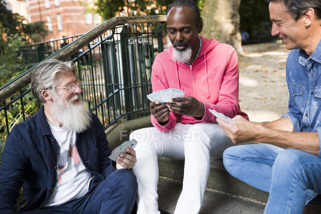 Three mature men sitting on steps and playing cards — Stock Photo