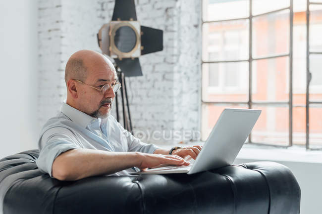 Homem sênior em poltrona usando laptop — Fotografia de Stock