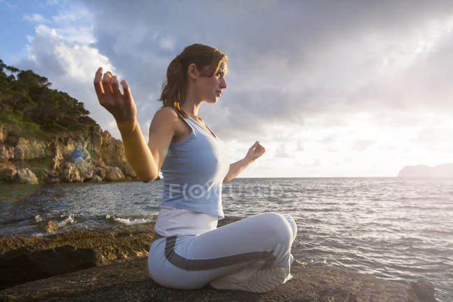 Mulher sentada em rochas por mar e meditando, Palma de Maiorca, Islas Baleares, Espanha, Europa — Fotografia de Stock