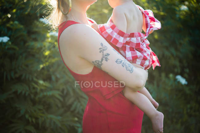 Mulher carregando bebê menina nos braços no jardim — Fotografia de Stock