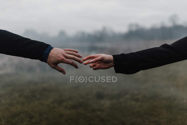 Обрезанный вид молодой пары, держащейся за руки, касающихся пальцев — стоковое фото