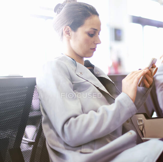 Young businesswoman in airport departure lounge looking at smartphone — Stock Photo