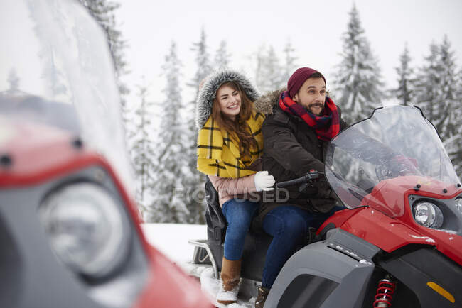 Pareja joven montando moto de nieve en invierno - foto de stock