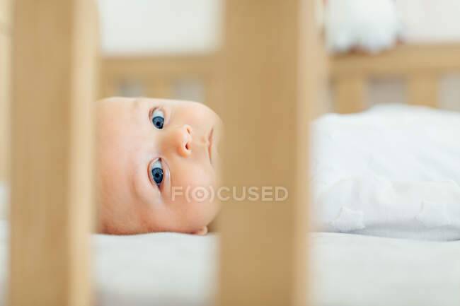 Вид через детскую кроватку лежащего мальчика, глядя в камеру — стоковое фото