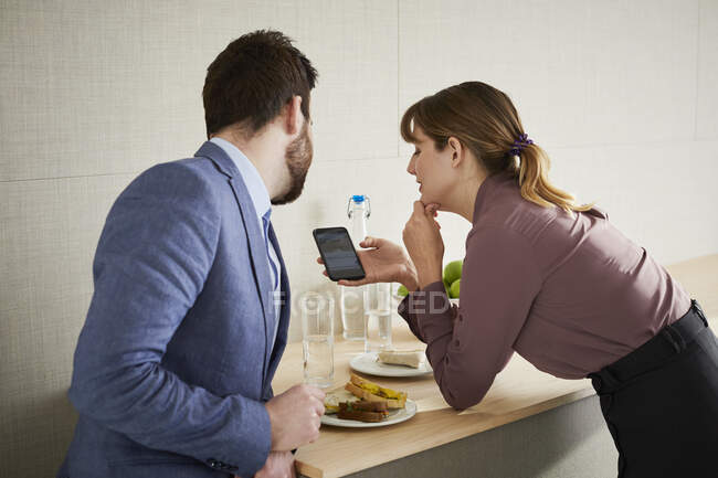 Коллеги обедают, смотрят на смартфон — стоковое фото