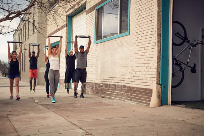 Grupo de personas con brazos levantados llevando equipos de pesas, vista frontal - foto de stock