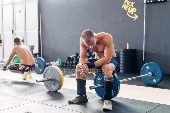 Exhausted man in gym sitting on barbell — Stock Photo