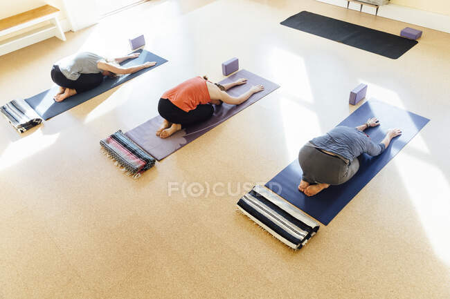 Trois femmes pratiquant la balasana (pose d'enfant) en studio de yoga — Photo de stock