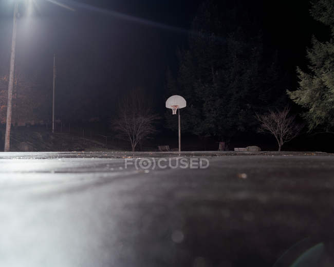 Пустой баскетбольный корт с баскетбольным кольцом ночью, на уровне поверхности — стоковое фото