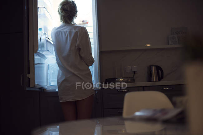 Visão traseira da mulher vestindo camisa olhando para a geladeira — Fotografia de Stock