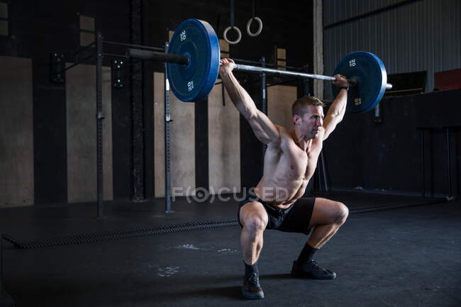 Homme faisant de l'exercice au gymnase, utilisant un haltère, position de squat avant — Photo de stock