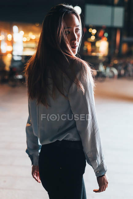 Retrato de mujer al aire libre en la noche mirando por encima del hombro - foto de stock