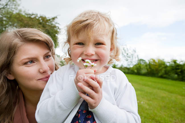 Mother and daughter in field and girl holding daisies — Stock Photo