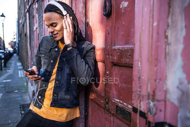 Человек на улице слушает музыку через наушники на смартфоне — стоковое фото