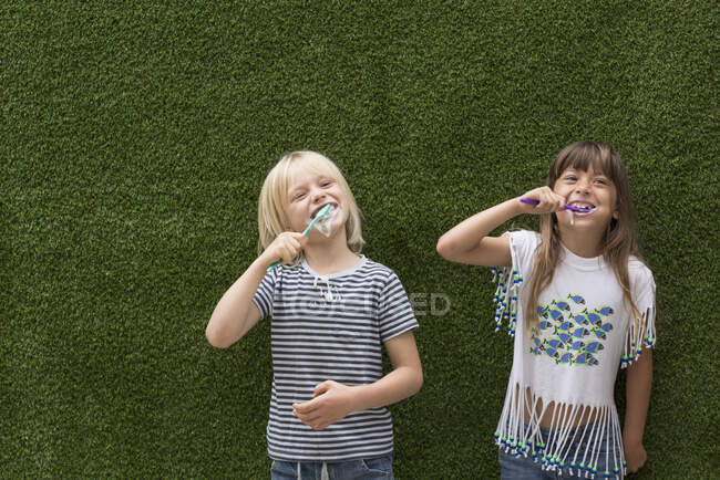 Two Children in front of artificial turf wall brushing teeth — Stock Photo