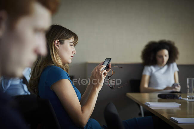 Femme d'affaires au bureau textos sur smartphone — Photo de stock