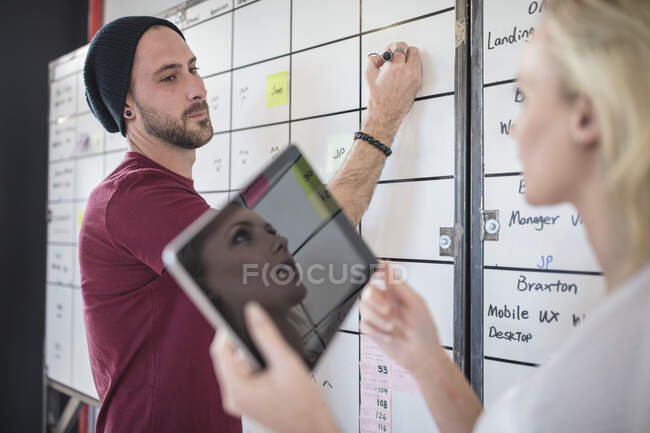 Male and female colleague planning  ideas on office whiteboard, over shoulder view — Stock Photo