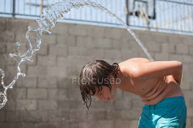 Vista laterale del ragazzo spruzzando acqua sul retro — Foto stock