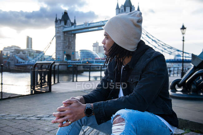 Young man sitting outdoors, pensive expressions, Tower Bridge in background, London, England, UK — Stock Photo