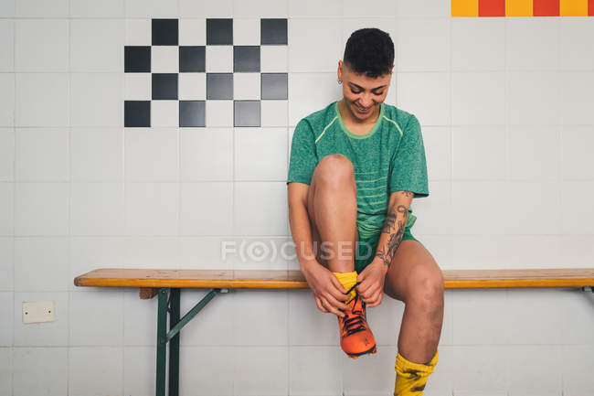 Female football player tying shoelace on bench in changing room — Stock Photo