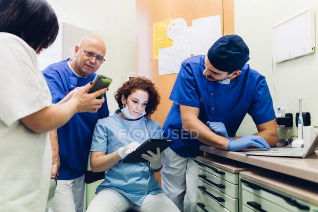 Dentistes dans le cabinet de dentiste regardant tablette numérique, ordinateur portable et smartphone — Photo de stock