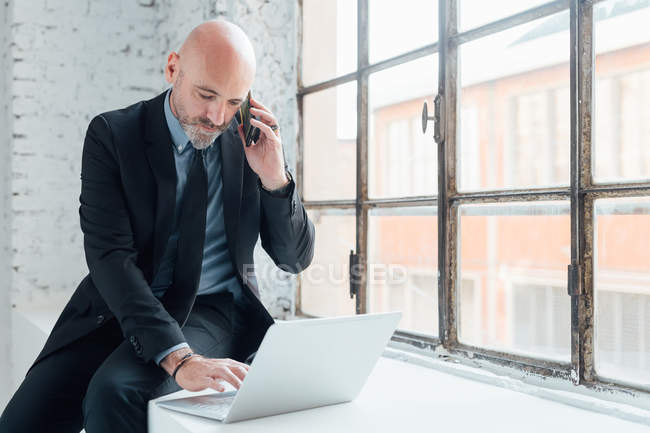Geschäftsmann auf Fensterbank mit Laptop und Smartphone — Stockfoto