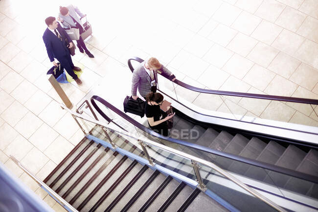Бізнесмени і жінки рухаються вгору ескалатор аеропорту, високий кут зору — стокове фото