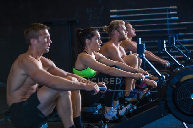 Group of people exercising in gymnasium, using rowing machines — Stock Photo