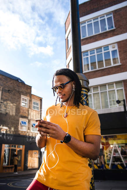 Junger Mann mit Kopfhörern nutzt Smartphone im Freien — Stockfoto