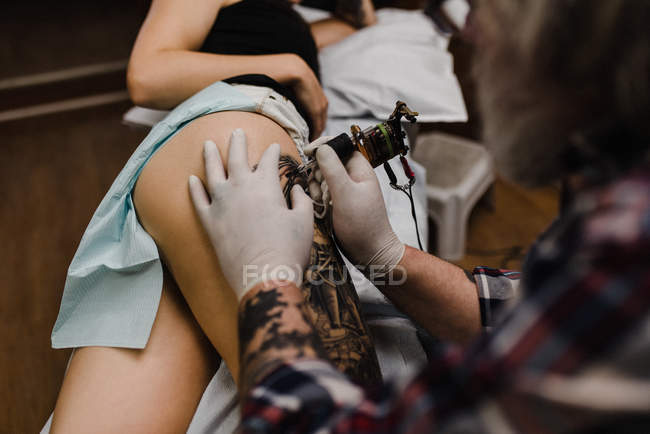 Close up de tatuador tatuando jovem mulher coxa — Fotografia de Stock