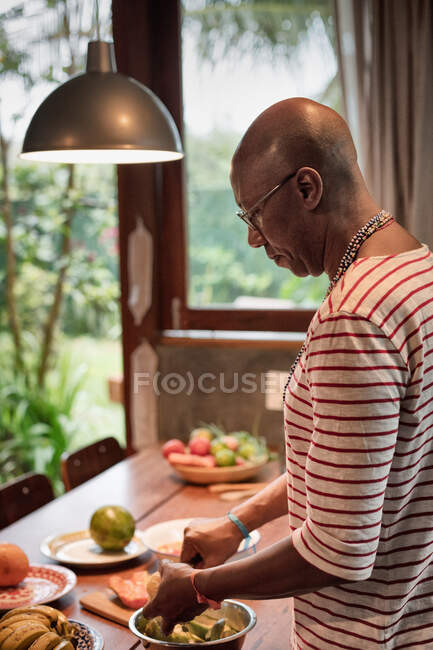 Homem maduro na mesa da cozinha preparando frutas na tigela — Fotografia de Stock