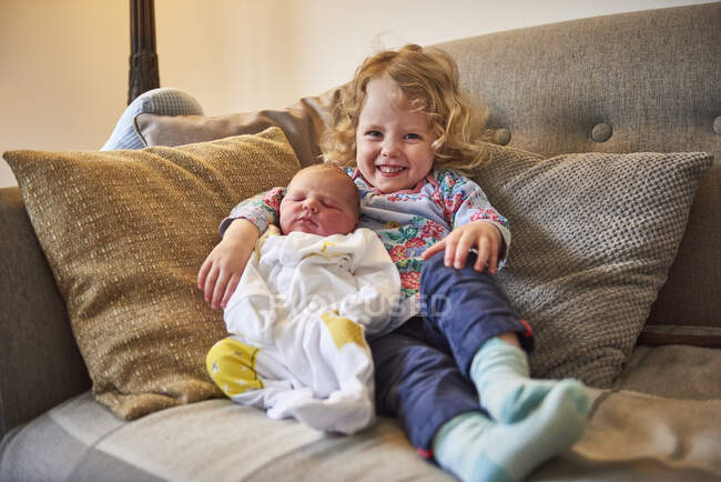 Female toddler and baby sister on sofa, portrait — Stock Photo