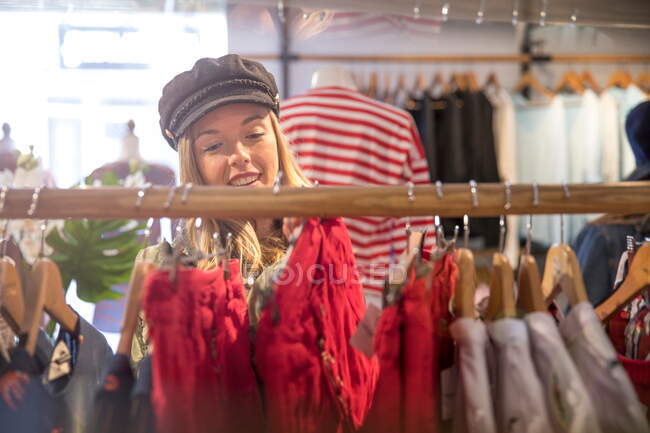 Parte anteriore vie di giovane donna esamina vestiti su rotaia in negozio — Foto stock