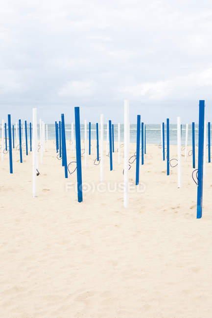 Polos de paraguas de playa blancos y azules en la playa de arena - foto de stock