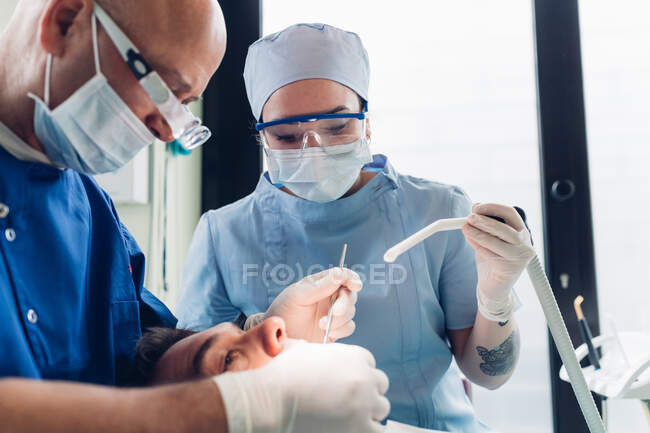 Dentista e enfermeiro dentário realizando procedimento odontológico no paciente masculino, close-up — Fotografia de Stock