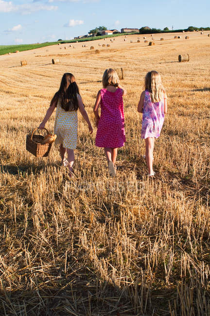 Three girls with bread in basket walking in field — Stock Photo