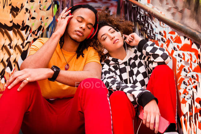 Two friends wearing headphones, listening to music, holding smartphone — Stock Photo