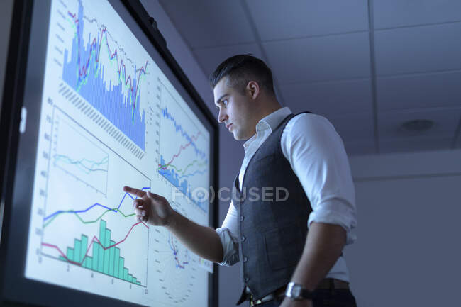Empresario viendo gráficos y gráficos en pantalla interactiva en reunión de negocios - foto de stock