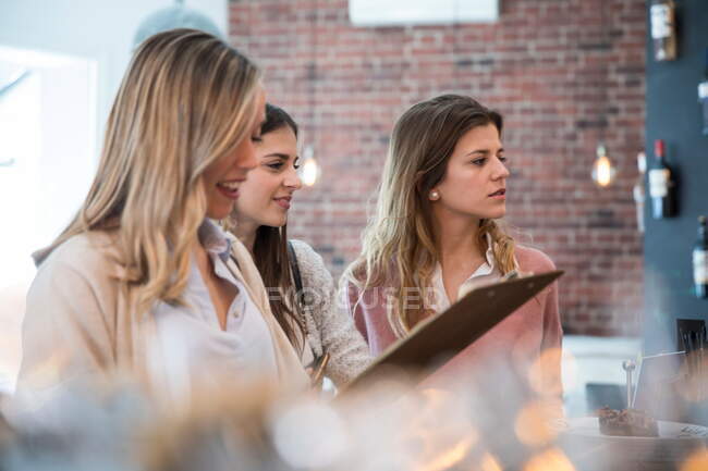 Three female friends, standing at counter in cafe — Stock Photo
