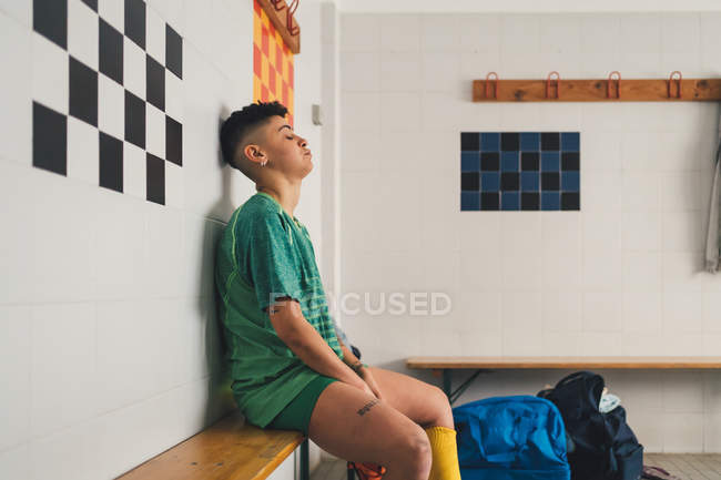 Female football player sitting on bench in changing room — Stock Photo