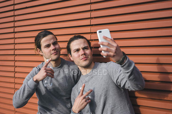 Jovens gêmeos do sexo masculino fazendo intervalo de treinamento e tirando selfie — Fotografia de Stock