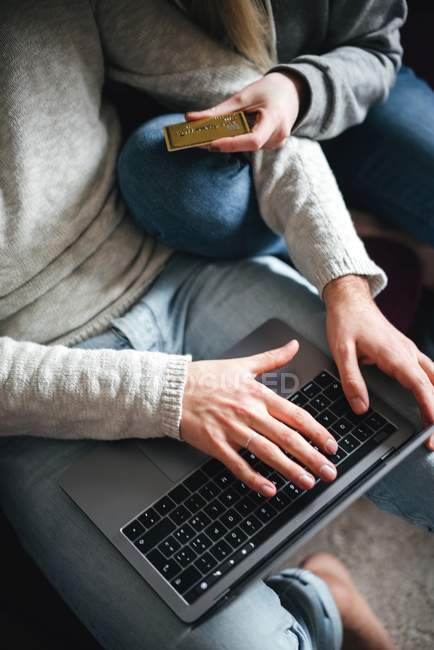 Пара с кредитной картой с помощью ноутбука, обрезанный вид — стоковое фото