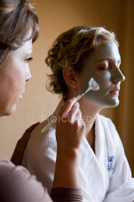 Woman having mud mask applying to face — Stock Photo