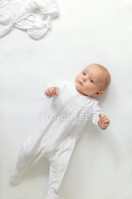 Overhead view of baby boy lying on white background looking away — Stock Photo