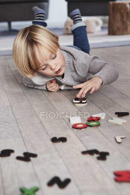 Giovane ragazzo sdraiato sul pavimento e accatastamento lettere magnetiche — Foto stock