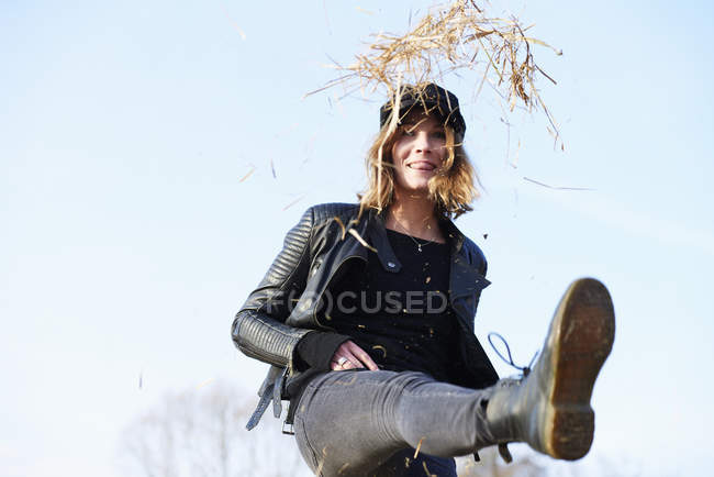 Woman in cap kicking up straw against blue sky — Stock Photo
