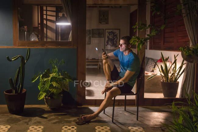 Mature man sitting on patio at night looking at smartphone — Stock Photo