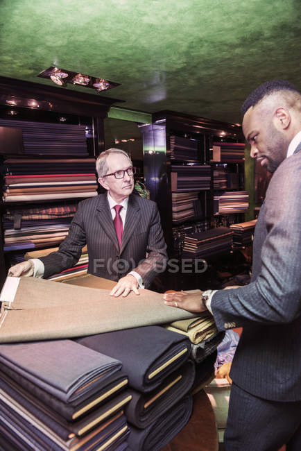 Senior tailor showing cloth to male customer in traditional tailor shop — Stock Photo