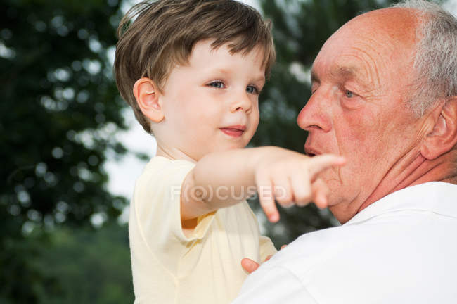 Retrato del abuelo con el nieto mientras el niño señala en algún lugar - foto de stock