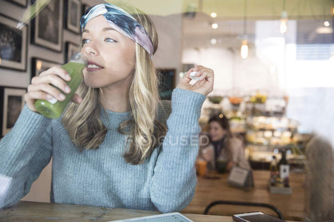 Young woman drinking vegetable juice at cafe window seat — Stock Photo